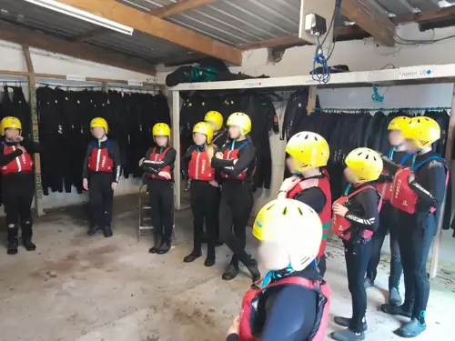 Young people in wetsuits, helmets and lifejackets in a wetsuit storage room